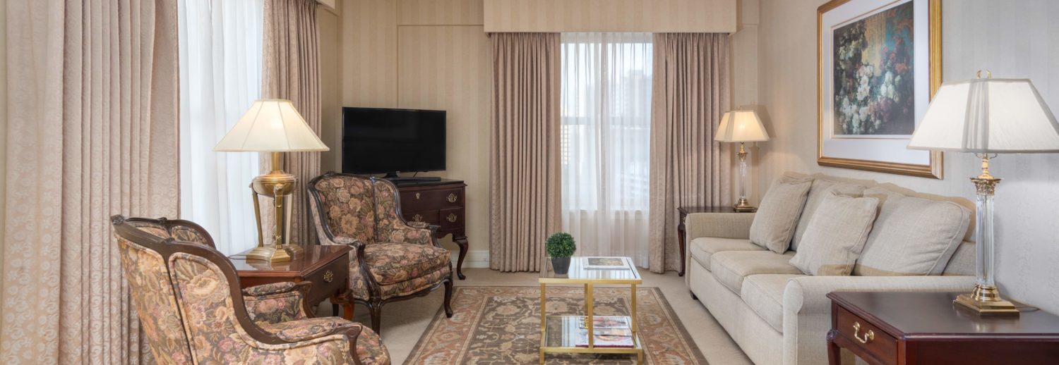 Sitting area of our Seattle hotel suite featuring large windows, chairs, tv, coffee table and sofa.