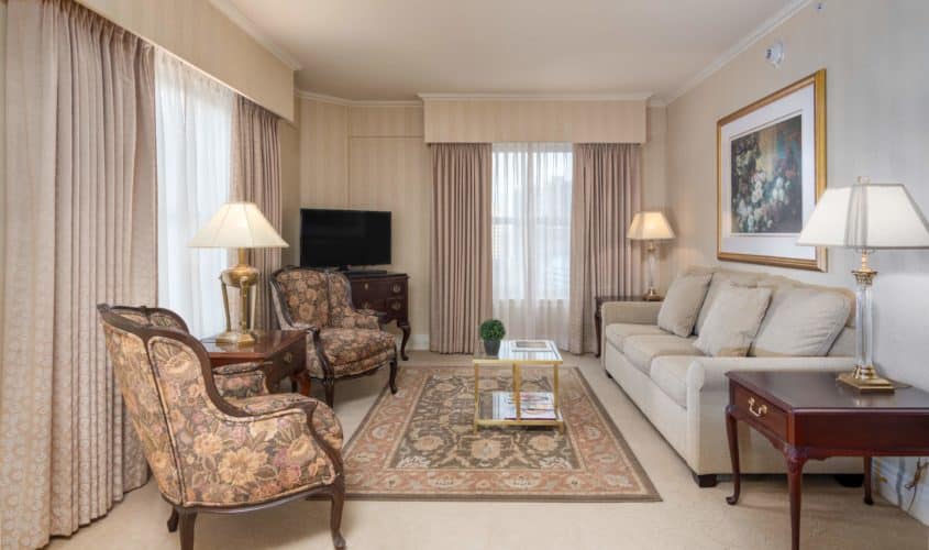 Sitting area of our Seattle hotel suite featuring large windows, chairs, tv, coffee table and sofa.