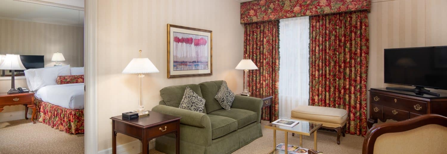 Spacious Seattle king hotel suite parlor with two large windows, red drapes and green couch