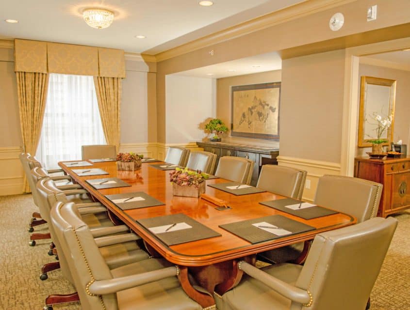 Board Room at Mayflower Park Hotel with wood table, plush seats & a window to bring in natural light