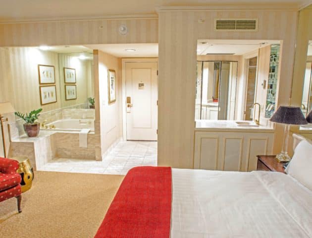 Seattle hotel king guestroom with spa featuring a large king bed, large spa tub, small bar area with a red chair on the side.