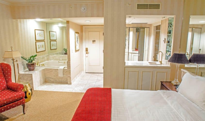 Seattle hotel king guestroom with spa featuring a large king bed, large spa tub, small bar area with a red chair on the side.