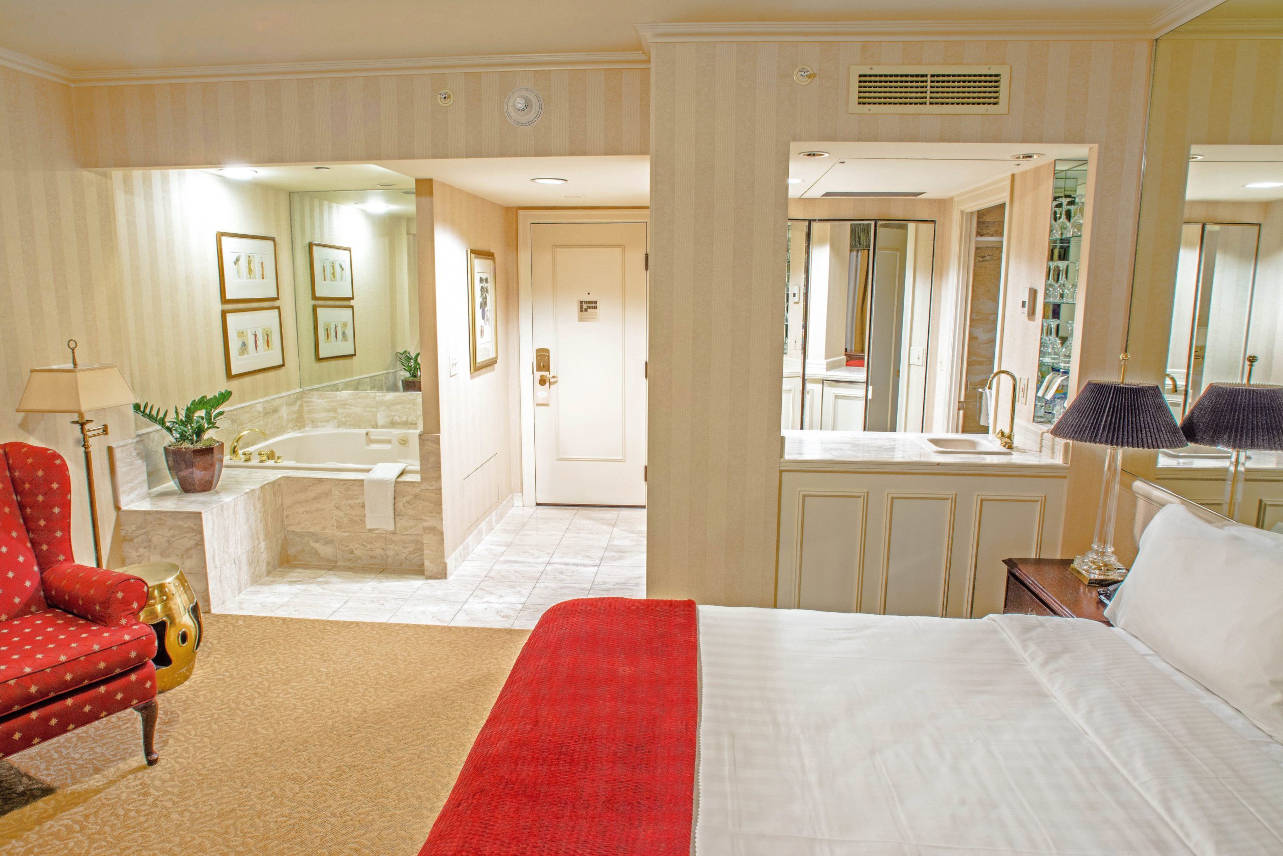 Seattle hotel king guestroom with spa featuring a large king bed, large spa tub, small bar area with a red chair on the side.