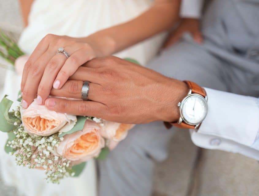 Couple holding hands with wedding rings over flowers