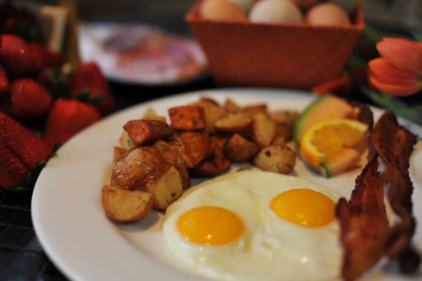 Close up of a plate of eggs, bacon, potatoes, and fruit for breakfast at Andaluca Restaurant.