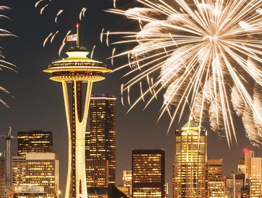 The historic Seattle Space Needle with the city buildings and meeting spaces in Seattle with fireworks set at night.